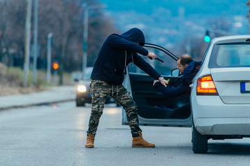 The car thief is pulling the car owner out of his car and trying to get the car while pointing a...
