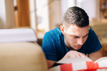 Handsome student studying on the couch with few opened books and a laptop next to him.