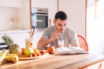 Obraz na płótnie Canvas healthy strong young man reading a book early in the morning while making his smoothie.