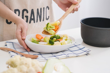 Woman in kitchen cooking stir vegetables on pan and tasting.