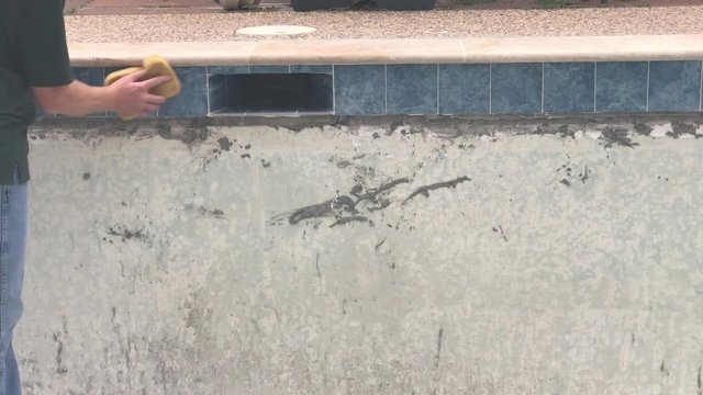 Construction worker wiping grout from tile in empty swimming pool