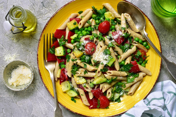 Penne pasta with vegetables : green pea, grilled bell pepper, tomato and zucchini. Top view with copy space.