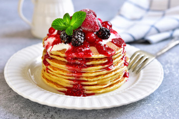 Stack of homemade delicious vanilla pancakes topped with sour cream,rasbberry syrup and berries.