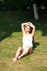 Obraz premium Young brunette woman in a turquoise blouse posing sitting on a green lawn in a summer park