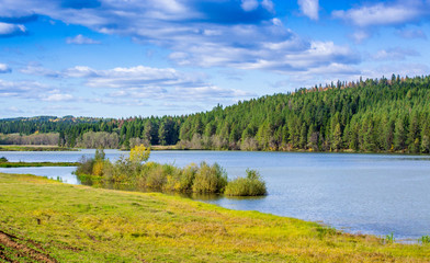 Beautiful lake, autumn forest on the shore and cloudy sky.