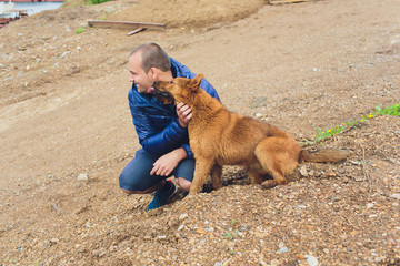 man on the beach, sand, hugging a dog, jacket.