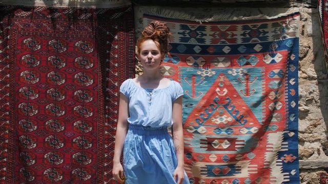 Beautiful tourist girl posing on street in front of old east oriental carpets.