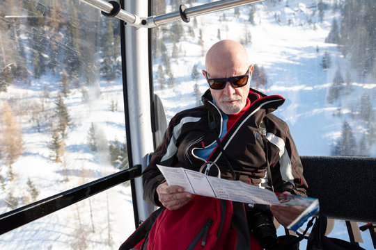 Senior man travelling in ski lift reading map