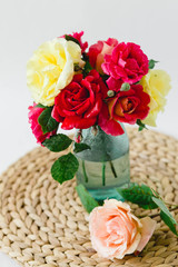 Coloful roses in vase on a wicker napkin on white background