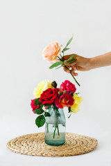 composition of colorful roses in a vase on a wicker napkin on a white background