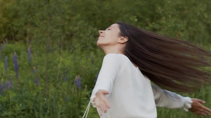 Free natural woman whirling around in green field. Young happy girl turns around circling with closed eyes outdoors nature background slow motion. Hair care products female ecological cosmetics