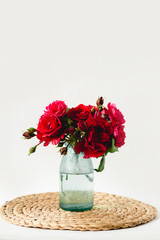 Coloful roses in vase on a wicker napkin on white background