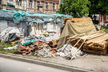 Big pile of house renovation and reconstruction construction leftover remains as junk and garbage on the street with wooden poles and planks near plastic bags and old roof tiles