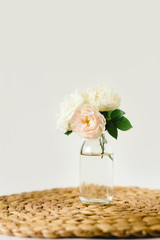 Beautiful roses in glass vase on a wicker napkin on white background