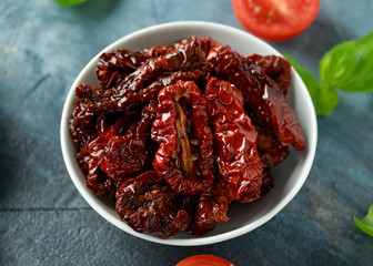 Sun dried tomatoes in white bowl with tomatoes and basil
