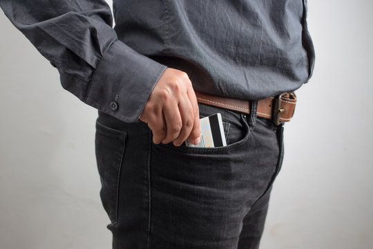 man putting a credit card in front pocket of dark blue jeans. Pocket of jeans staffed with credit card, denim background.