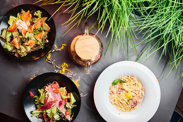 Pasta carbonara, vegetable salad with prosciutto and vegetable salad with salmon on a gray-smoked background top view. Close up