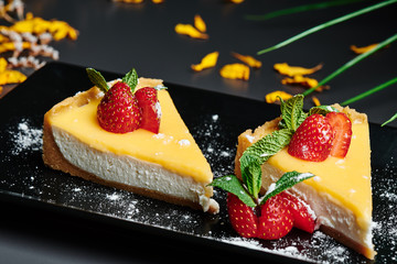 Delicious Cheesecake, decorated with strawberries on a square black plate in a dark background decorated with beautiful greenery. Close up. Space