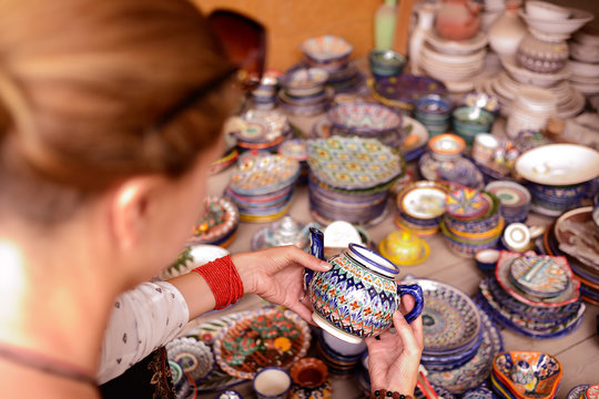 Watching tourist handmade colourful ceramic pottery with jug and cups selling at street stall in Rishton, Uzbekistan