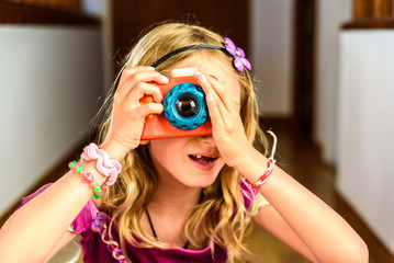 Little girl playing with a colorful photo camera toy made of wood.