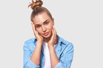 Portrait of charming young woman touching her perfect soft face skin with hands, posing over white background. Pretty female using face cream, healthy beauty skin cosmetic concept. People, healthcare