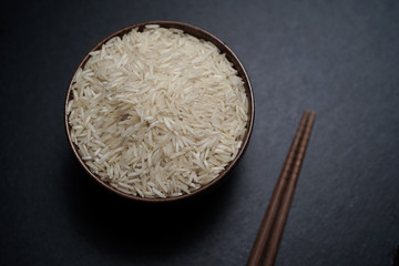 Rice inside wooden bowl on top of black stone plate with wooden matt