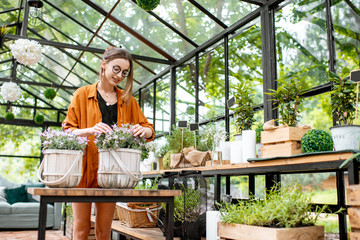 Young woman taking care of plants, growing herbs and flowers in the beautiful greenhouse