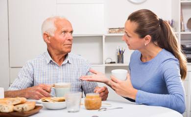 Fototapeta na wymiar Mature man with daughter talking at table with cup of tea