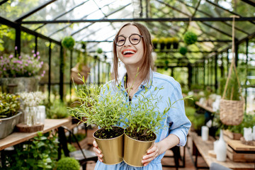 Portrait of a young woman standing with herbs at the entrance of the beautiful greenhouse or flower shop