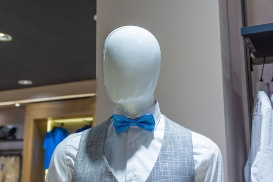 White mannequin in a fashion store with grey vest and blue bow tie.