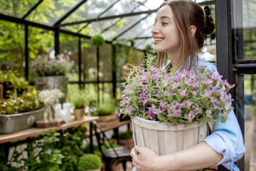 Portrait of a young woman standing with lavender at the entrance of the beautiful greenhouse or flower shop