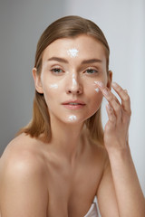 Skin care. Woman applying facial cream on beauty face closeup