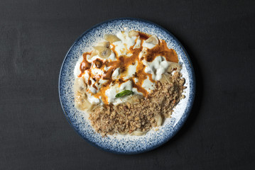 Traditional Turkish meat pasty with yoghurt,sauce,spices and walnuts in a blue colored dish on a black background with scratches