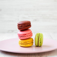 Sweet and colorful macarons on pink plate over white wooden background, side view. Close-up.
