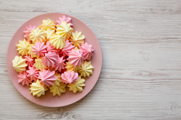 Mini meringues on a pink plate over white wooden surface, overhead view. Close-up. Copy space.