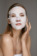 Facial mask. Woman using sheet mask on face skin for spa care