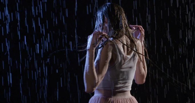 Attractive young blonde woman in white top flips long hair side to side in night rain. Medium shot. Slow motion 4K recorded at 60fps