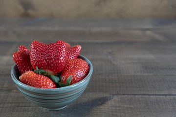 Ugly fruit. Funny strawberry in a bowl on brown wooden background. Close up. Copyspace for text