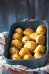 Baked potatoes with oil and spicy herbs in a blue pan, selective focus, blurred background.
