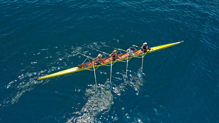 Aerial drone bird's eye view of sport canoe operated by team of young women in deep blue sea waters