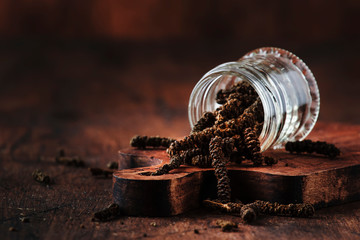 Fragrant long pepper spilling out of glass jar, vintage kitchen table background, selective focus