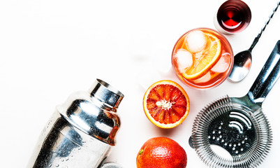 Popular alcoholic cocktail Negroni with dry gin, red vermouth and red bitter, orange and ice cubes. White background, bar tools, top view, place for text.