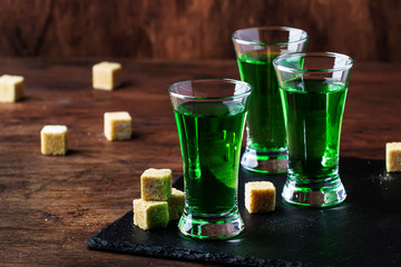 Absinthe - strong alcoholic drink, green bitter wormwood tincture in glasses on the old wooden table, place for text