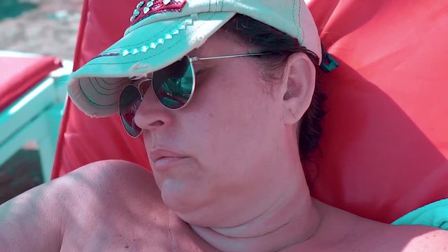 Caucasian woman in hat relaxing and sleeping on the beach. She wearing sunglasses