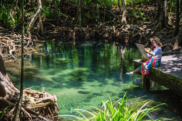 Naklejka na ściany i meble Asian women travel relax, travel nature in the holiday. women enjoying Sitting and watching the travel map the lake mangrove forest. tha pom-klong-song-nam at krabi. summer, Map