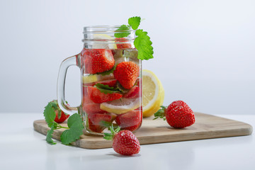Mug of fruit water with strawberries, mint and lemon, stand on a wooden stand next to fresh strawberries, mint leaves and sliced lemon, top view.