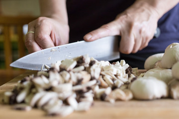 A woman cuts mushrooms with a knife on a wooden cutting board