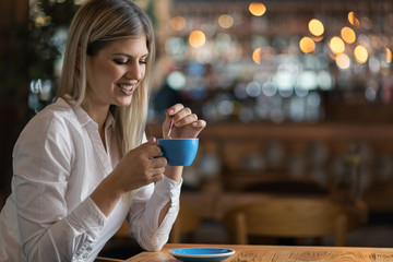 Happy young woman thinking of something while drinking coffee in a cafe
