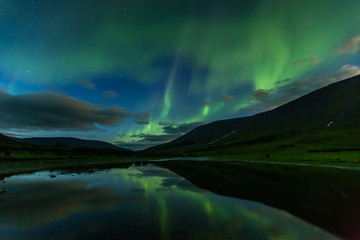 aurora borealis in the night sky cut the mountains, reflected in the water.