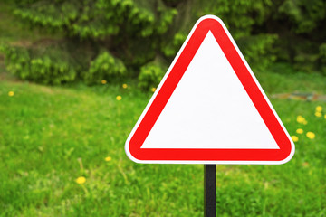 Empty red triangle road sign with not text and sign on the street and green trees in the background